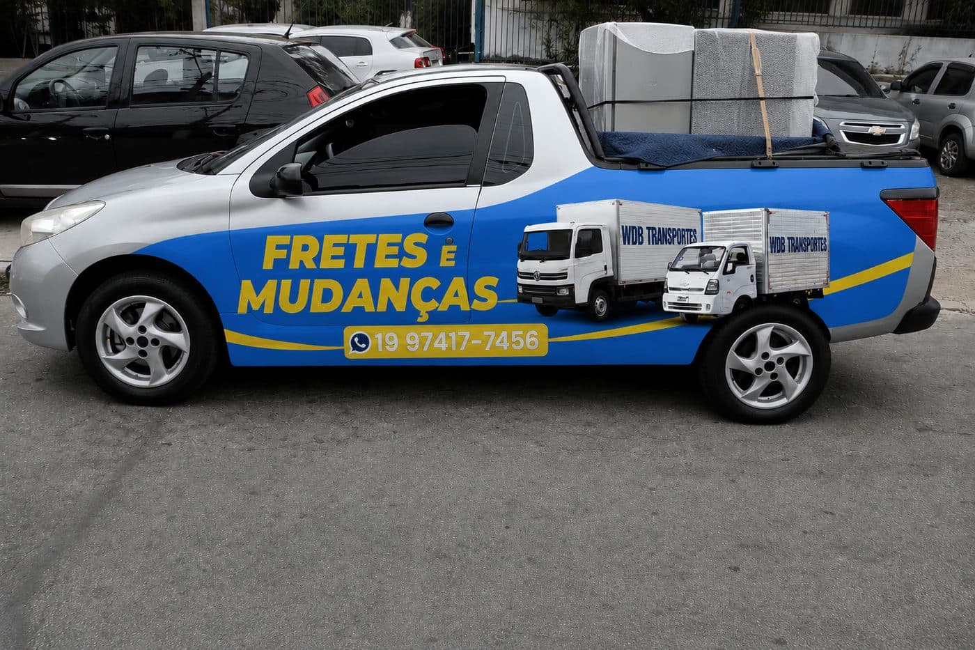Picape adesivada da WDB, de lado, com eletrodomésticos embalados em plástico bolha e amarrados sobre cobertor na caçamba